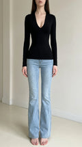 Front view of woman wearing black deep v-neck long sleeve top with light wash jeans