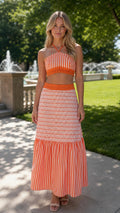 Front view of woman wearing orange halter crop top and matching tiered maxi skirt