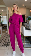 Front view of woman wearing magenta off-the-shoulder jumpsuit with white sneakers