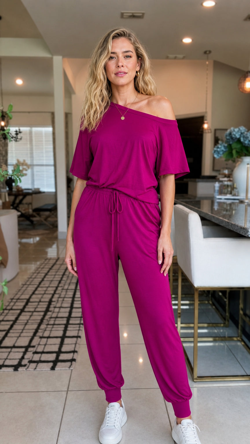 Front view of woman wearing magenta off-the-shoulder jumpsuit with white sneakers