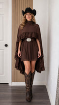 Front view of woman wearing brown mock neck ruffle cape mini dress with cowboy hat and boots