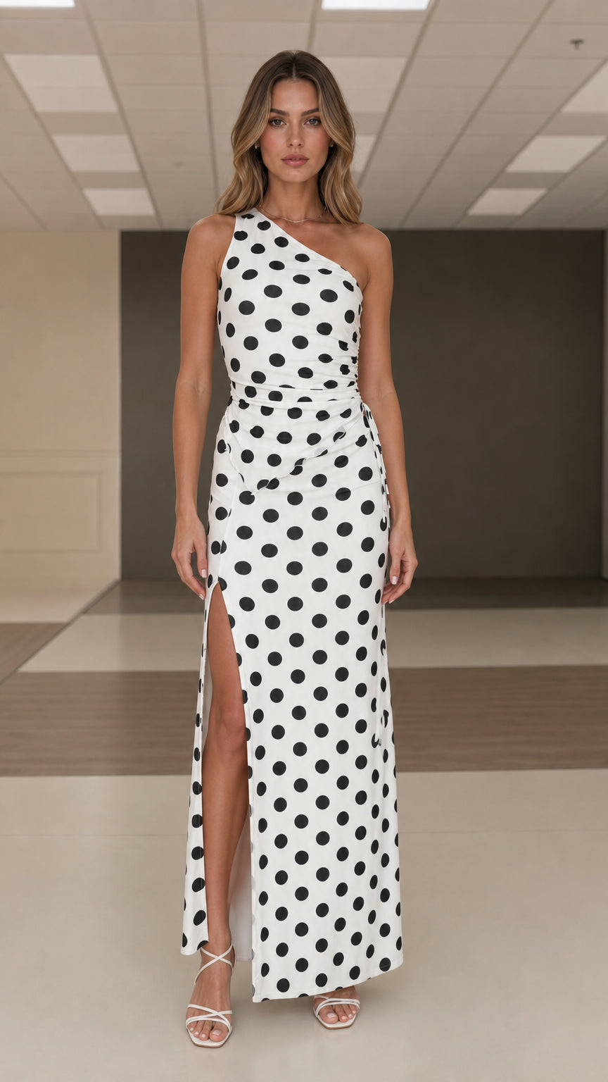 Front view of woman wearing white and black polka dot one shoulder maxi dress with slit