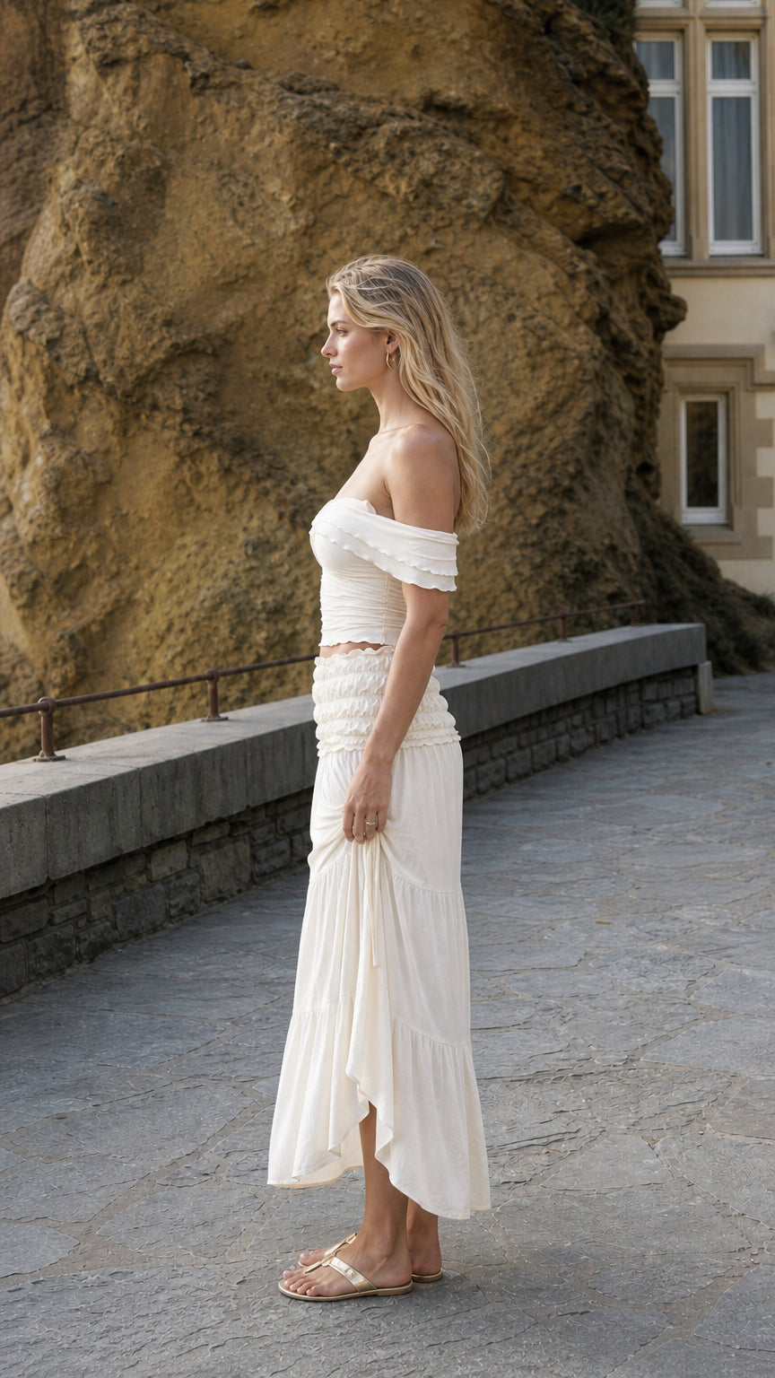 Side profile view of woman in ivory two-piece set standing near stone wall