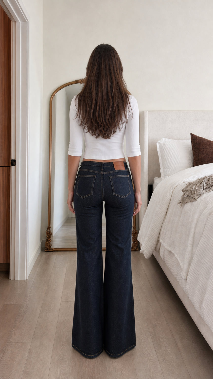 Back view of woman wearing white ribbed cropped top and dark denim flare jeans