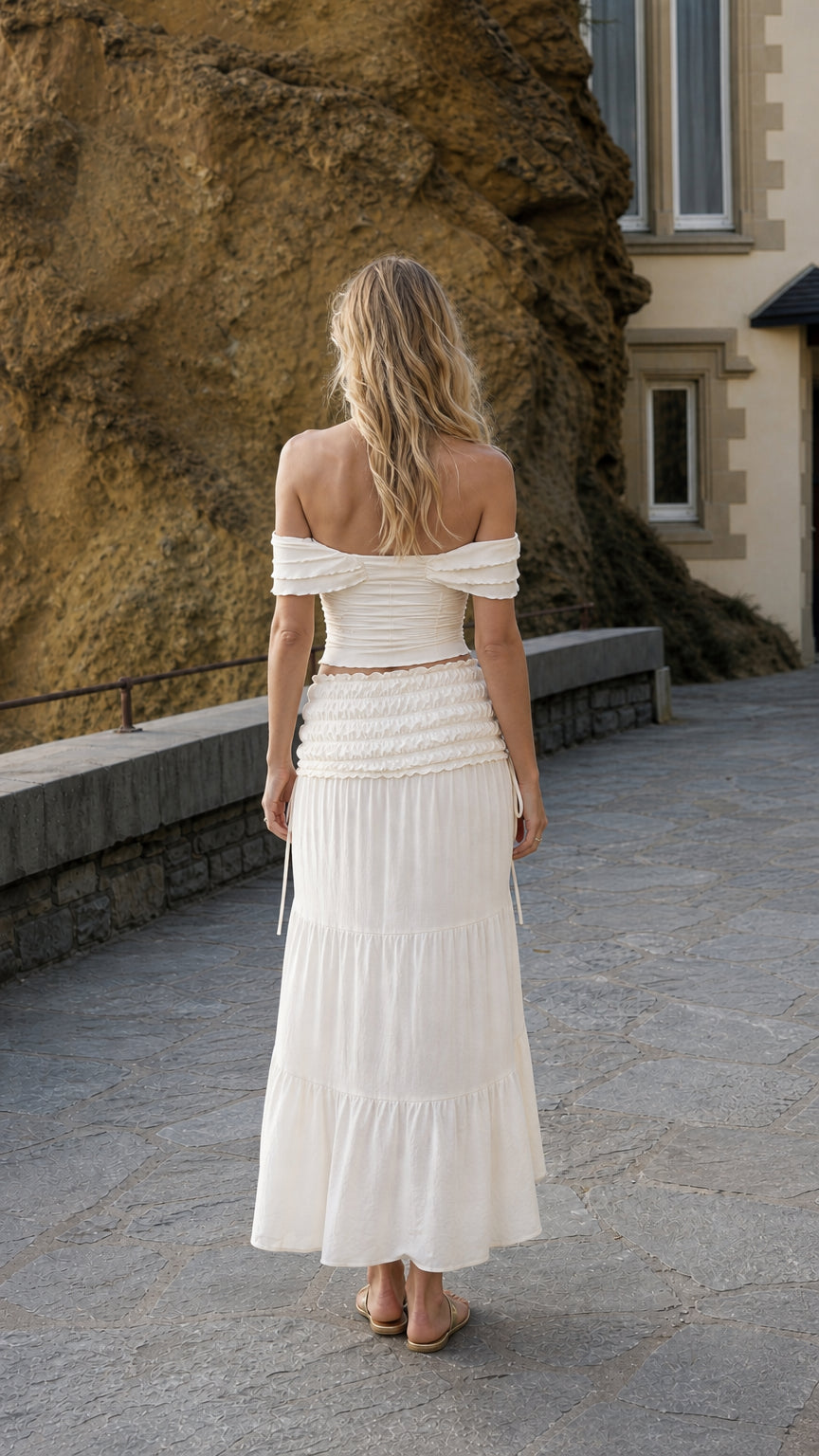 Back view of woman wearing ivory off-shoulder top and matching skirt