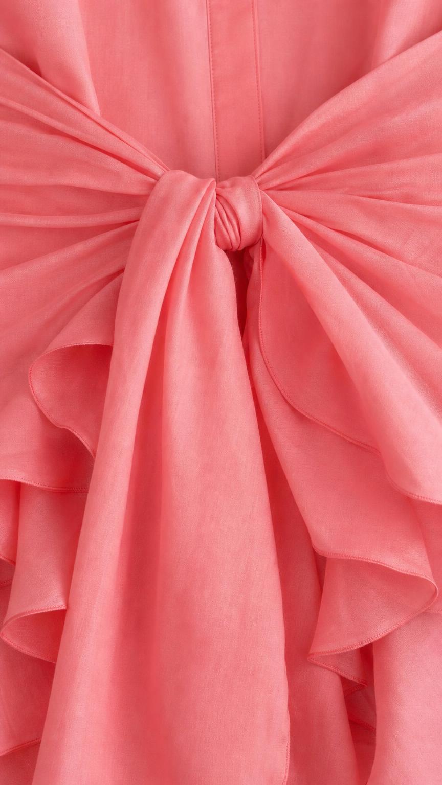 Close-up of the tie-front knot and ruffle hem detail on coral dress