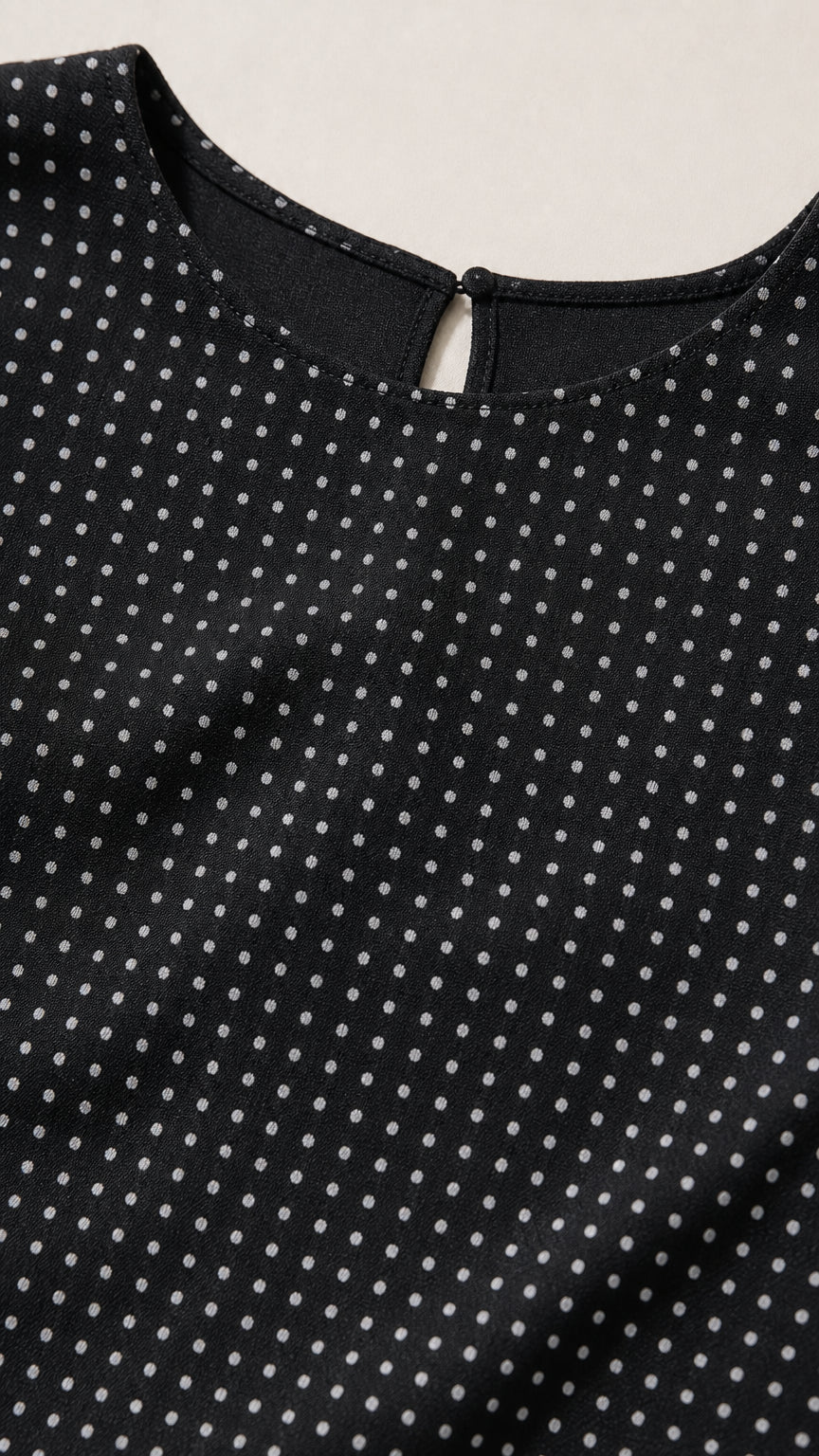Close-up detail of black fabric texture and neckline with button closure