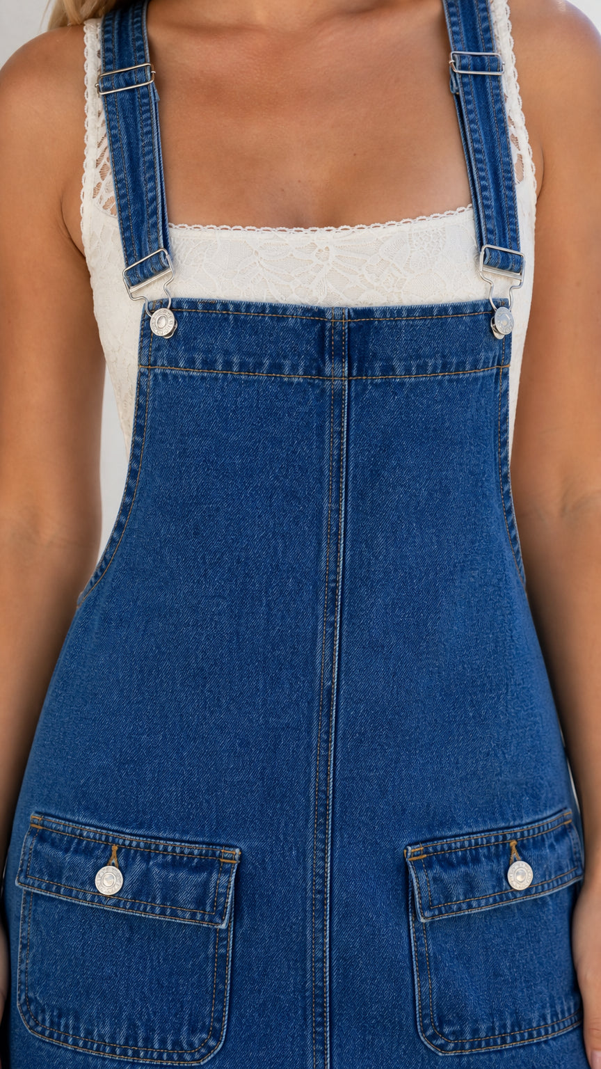 Close-up detail of straps, buttons, and front pockets on blue denim overall dress