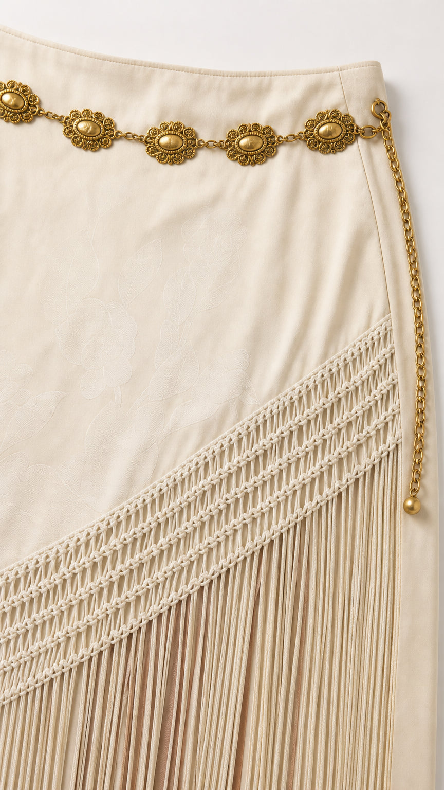 Close-up of decorative metal belt and woven fringe detail on beige skirt